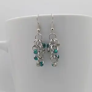 Silver dangly earrings with clear and teal beads hanging on a white mug.