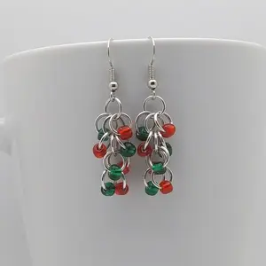 Silver dangly earrings with emerald and red beads hanging on a white mug.