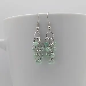 Silver dangly earrings with green beads hanging on a white mug.