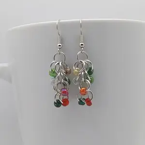 Silver dangly earrings with holiday mix beads hanging on a white mug.