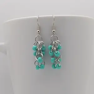 Silver dangly earrings with opaque turquoise beads hanging on a white mug.