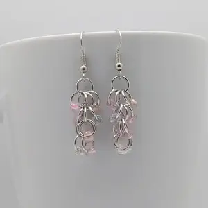 Bright silver aluminum chain mail earrings with pink mist beads on a white mug.