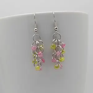 Bright silver aluminum chain mail earrings with pink and yellow beads on a white mug.