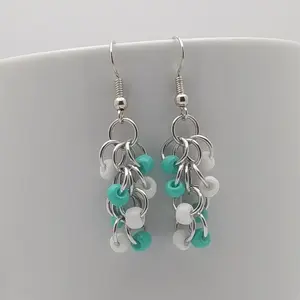 Bright silver aluminum chain mail earrings with white and turquoise beads on a white mug.