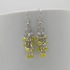 Bright silver aluminum chain mail earrings with yellow luster beads on a white mug.