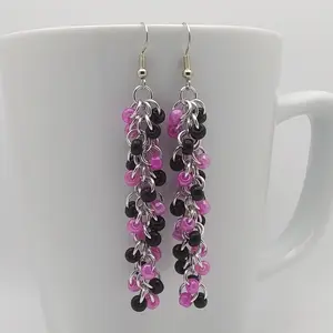 Bright silver aluminum dangly chain mail earrings with a swirl of black and dark pink beads on a white mug.