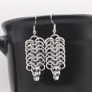 Bright silver aluminum chain mail earrings on a black mug.