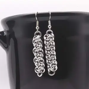 Bright silver aluminum chain mail earrings on a black mug.